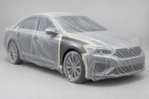 Translucent automotive overspray masking film covering a sedan with a taped front-fender repair opening