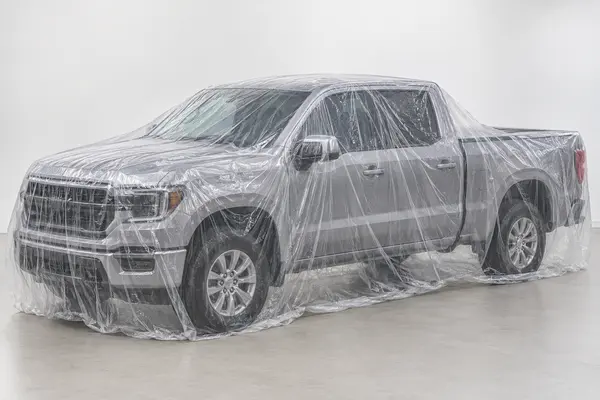 Transparent disposable plastic full-car cover fitted over a generic crew-cab pickup truck