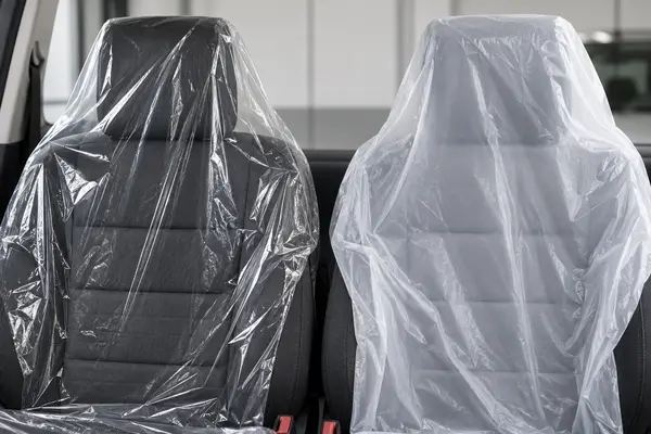Close comparison of transparent and milky-white disposable automotive seat-cover film on dark seats