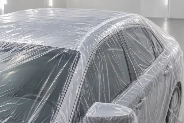 Transparent disposable full-car cover showing a sealed seam under light tension over a sedan roof