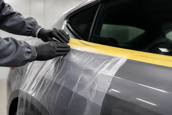 Pre-taped automotive masking film applied along a car window and door panel
