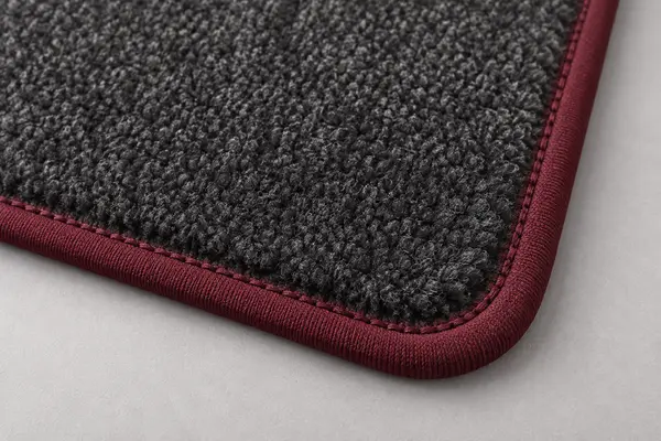 Close view of burgundy textile binding and even stitching around a charcoal wool automotive floor mat